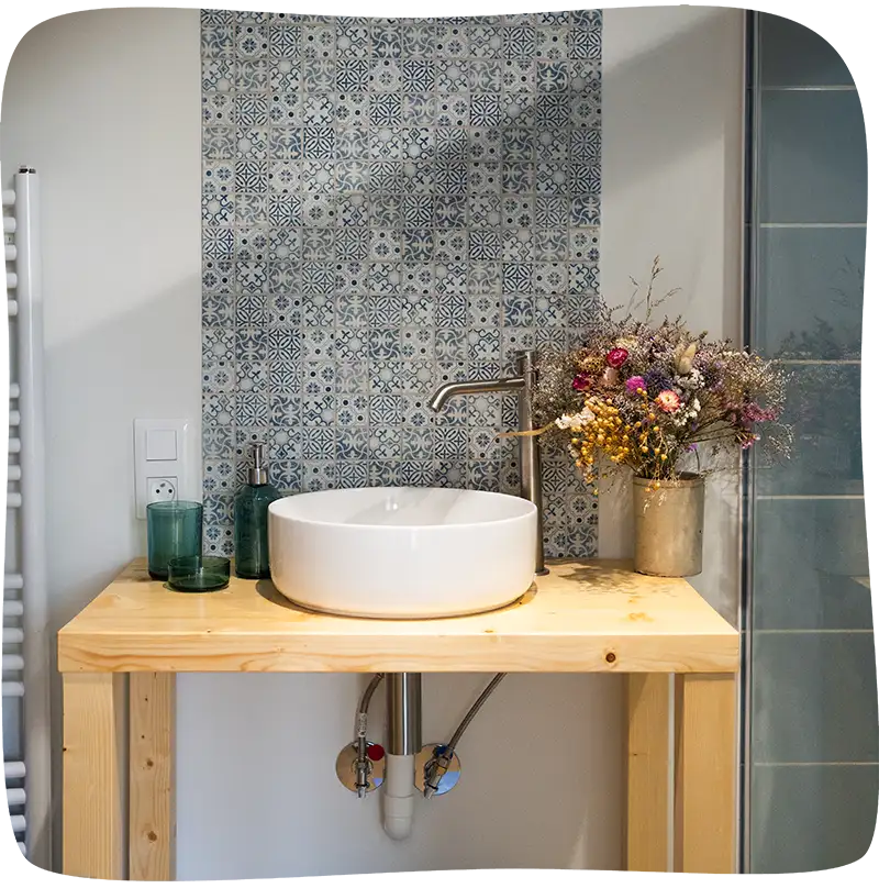 Chambre 1 - Evier sur un meuble en bois de 70cm avec un pot de fleurs séchées au fond à droite du meuble