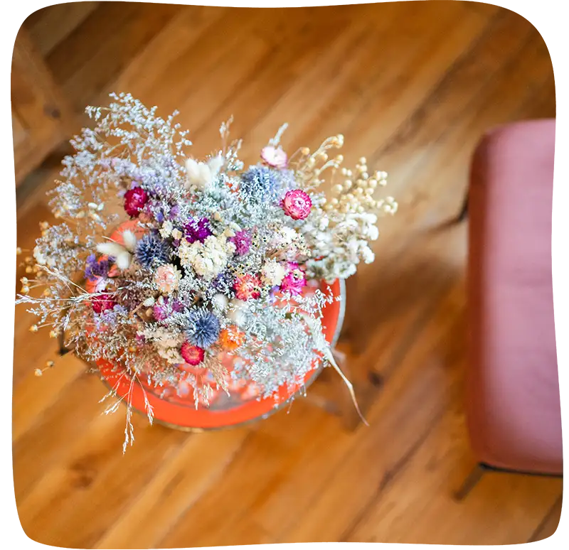 Bouquet de fleurs séchées sur un tabouret rouge vu de haut. On apercoit un début du fauteuil sur la droite