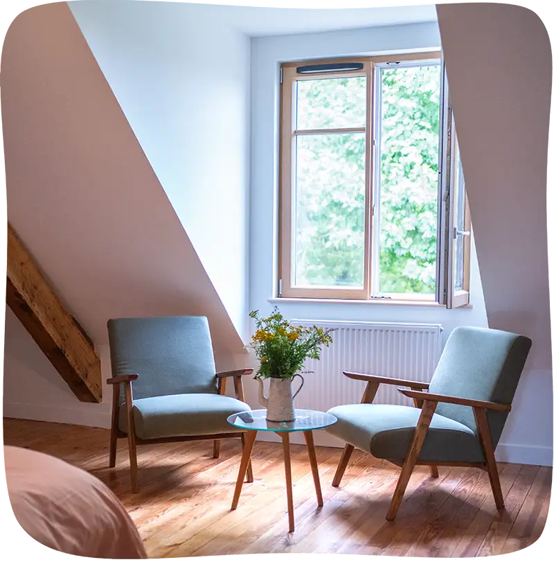 Deux fauteils verdeau dans une table basse en verre avec un pot de fleur par dessus. Ces fauteuils sont devant une grande fenêtre limuneuse double dont la partie droite est grand ouverte.