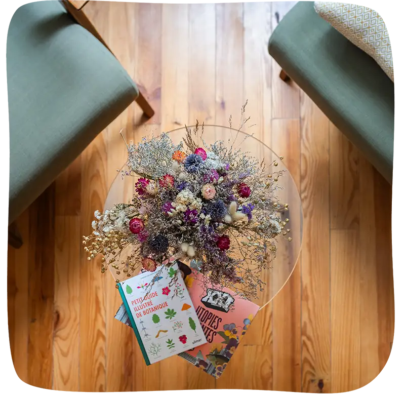 Vue aérienne d'un pot de fleurs et de deux bouquins se trouvant sur une table en verre. On peut apercevoir le début des deux fauteuils sur les bords haut gauche et haut droit.