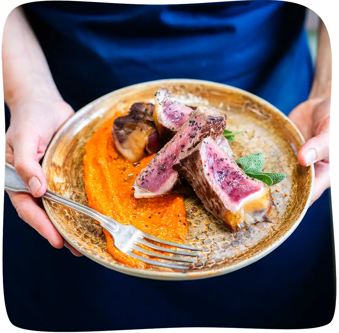 Assiette remplie de viande, une purée de carotte et d'une fourchette dans tenue dans des mains