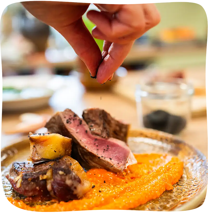 Main qui laisse tomber des épices dans une assiette de viande sur un lit de purée de carotte