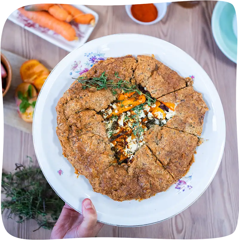 Omelette bretonne dans une assiette blanche avec des motifs de fleurs vue de haut au dessus d'une table remplie d'ingrédients pour cuisiner