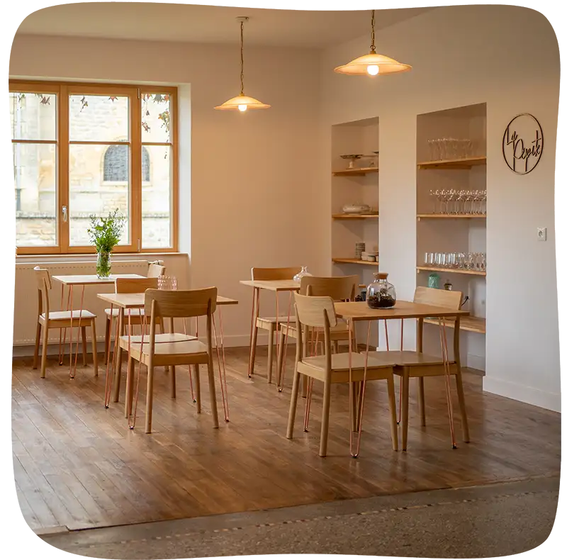 La pièce où les invités mangent. Les peintures sont claires, la pièce est lumineuse et deux lustres complètent la lumière avec des ampoules à lumière chaude. On retrouve 4 tables de deux personnes en bois sur un parquet en bois. Dans le fond à droite dans un renfoncement du mur se trouvent les verres.