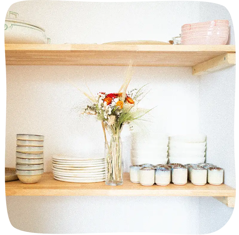 Présentation des assiettes, bols et tasses sur les étagères dans un renfoncement avec un vase et des fleurs dans les tons rouges, orange et blanc au milieu