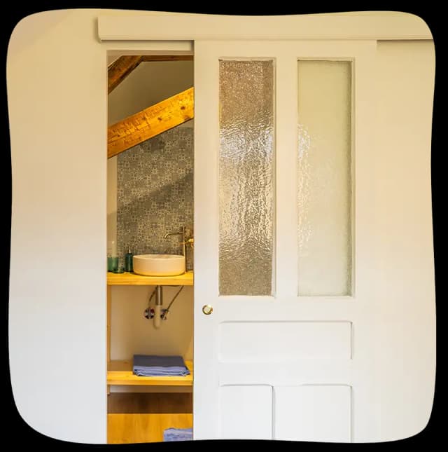 Chambre 1 - Porte entrouverte donnant sur la salle de bain. On peut apercevoit l'évier et un morceau de la charpente en bois