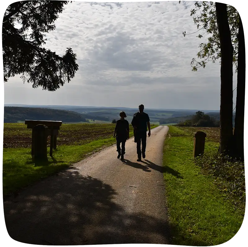 2 personnes qui marchent en sortie de forêt sur une route en beton.